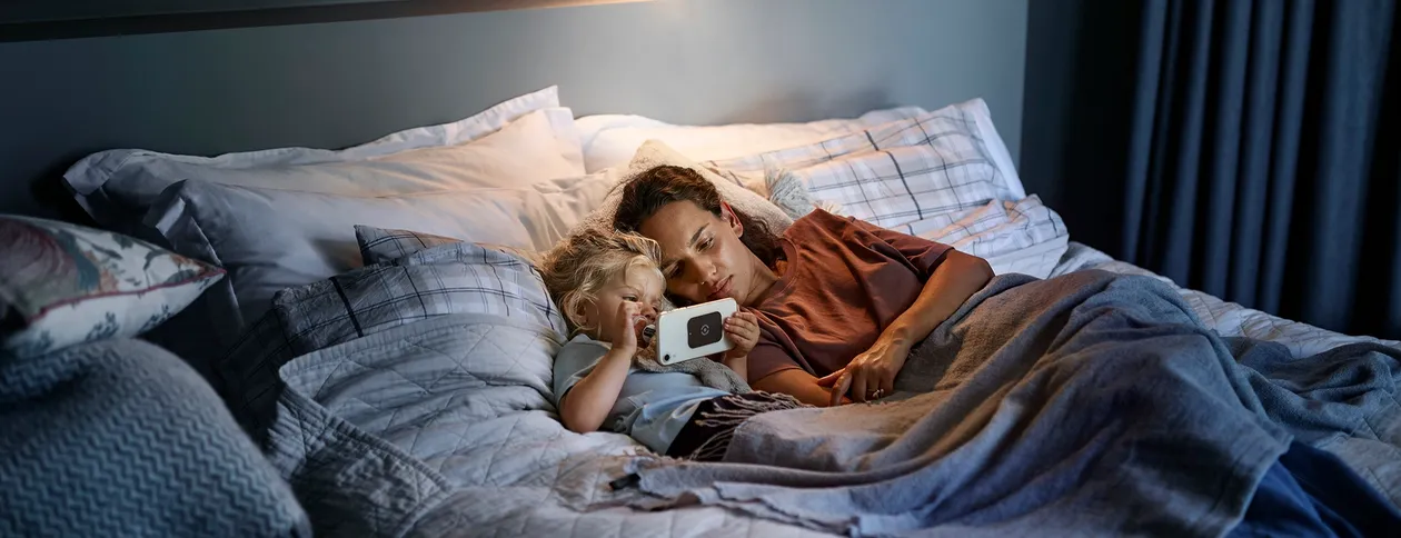 Mor og barn som ser på en smarttelefon i senga